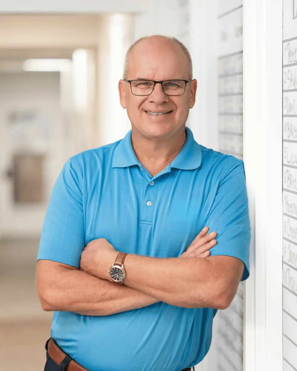 Dave Petkovsek in a blue polo shirt, arms crossed, smiling in the hallway of the Realty Exchange office